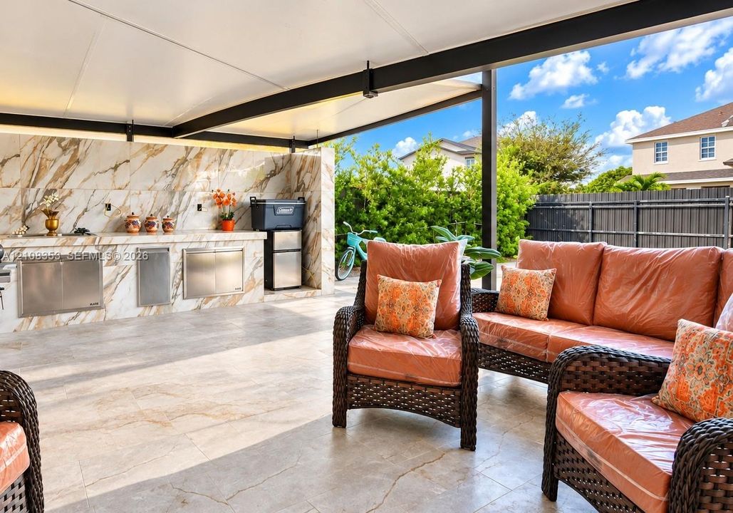 Covered outdoor patio featuring large-format tile flooring, a stone-finish backsplash, and integrated stainless steel cabinetry