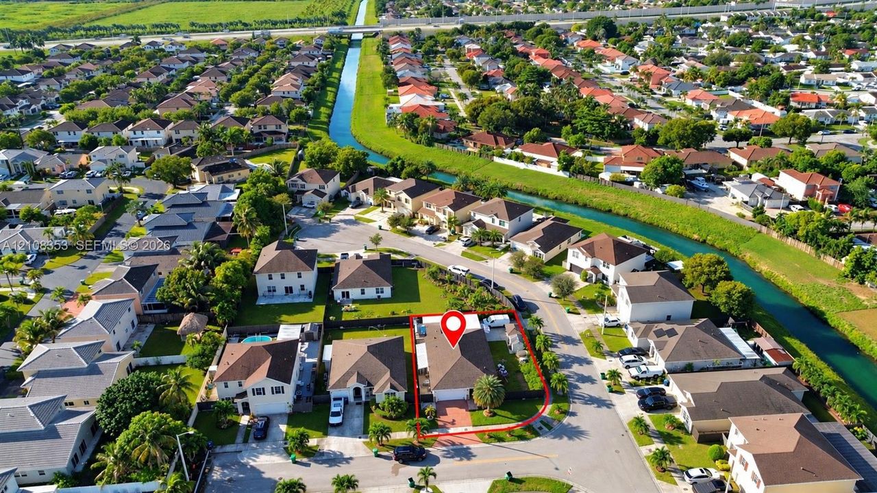 Aerial perspective of a residential property featuring a hipped roof structure, an attached garage, a paved driveway, and a fenced perimeter