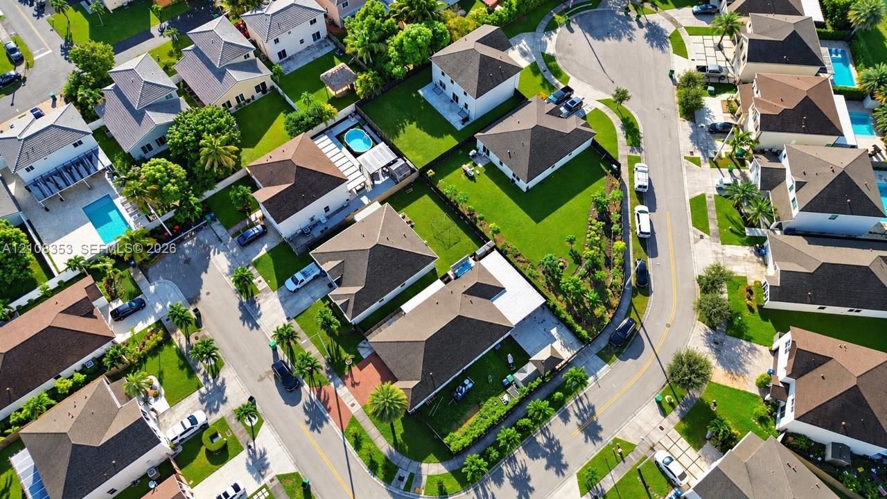 Aerial perspective of a suburban neighborhood featuring residential lots, paved streets, manicured lawns, and private swimming pools