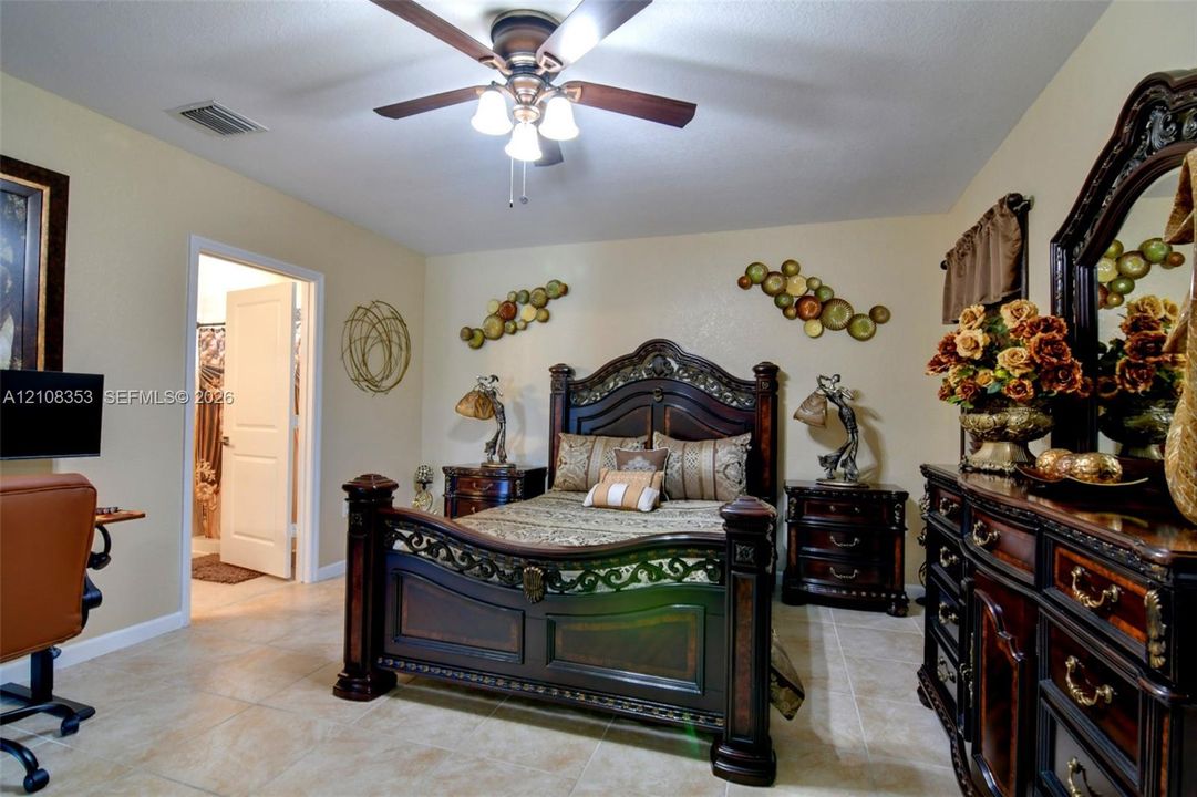 Spacious room featuring neutral tile flooring, a multi-blade ceiling fan with integrated light fixture, and a solid-core interior door