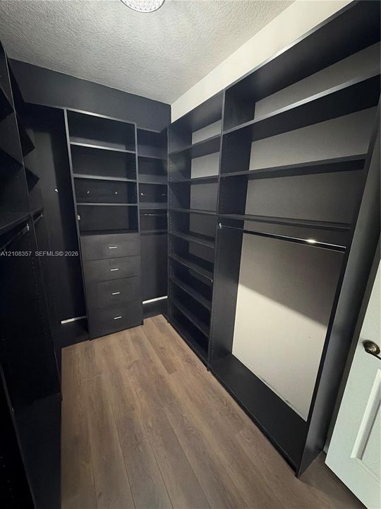 Custom walk-in storage featuring dark finish floor-to-ceiling cabinetry, integrated shelving, built-in dresser drawers, and wood-finish flooring