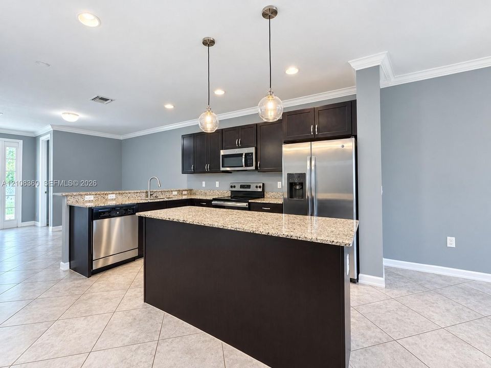 Kitchen featuring dark cabinetry, stone-surface countertops, stainless steel appliances, a central island, and globe pendant lighting