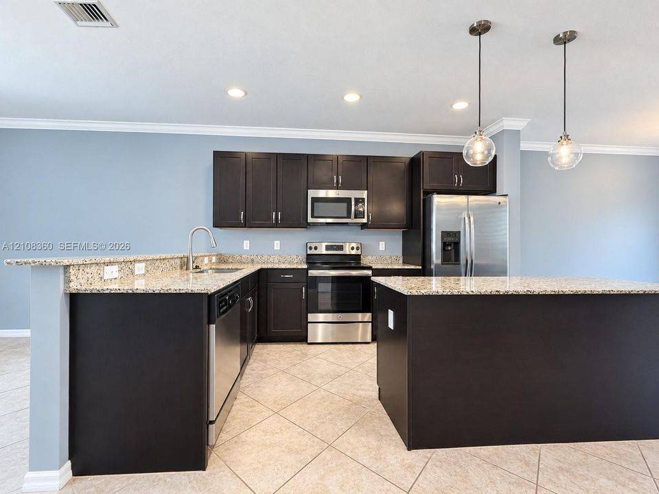 Kitchen featuring dark wood cabinetry, stone countertops, stainless steel appliances, a peninsula island, and globe pendant lighting