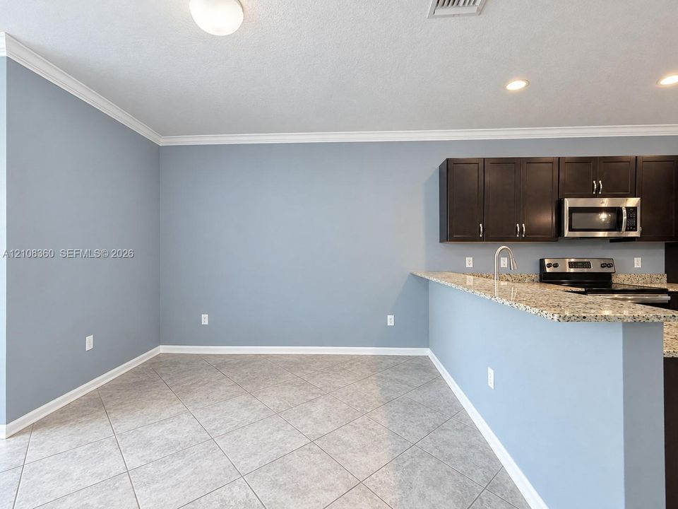 Kitchen area featuring dark cabinetry, speckled stone countertops, stainless steel appliances, tile flooring, and crown molding