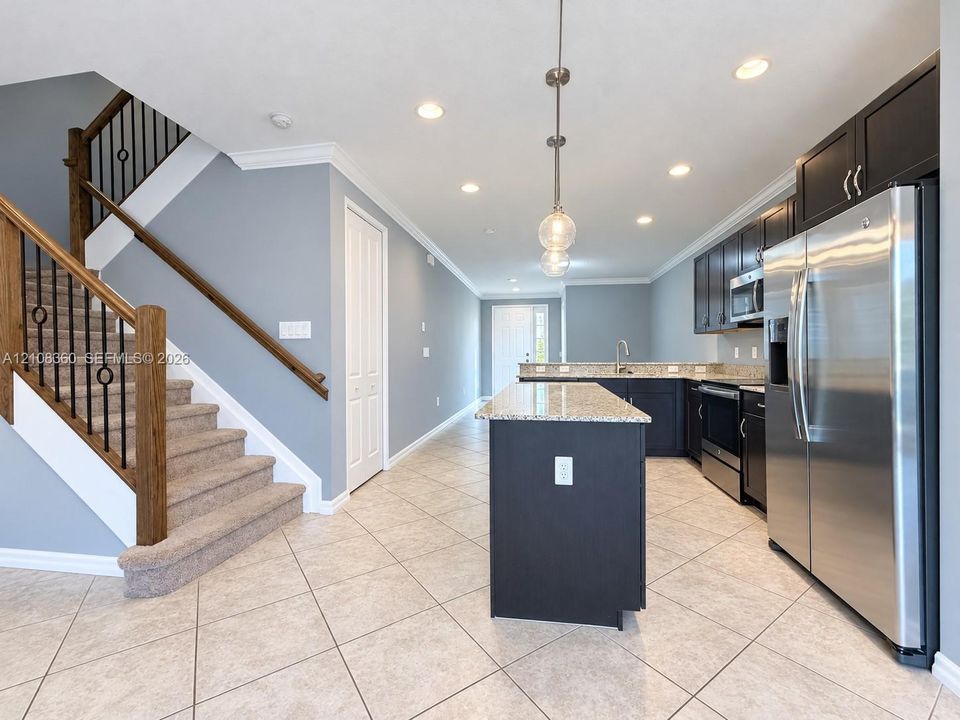 Kitchen featuring dark cabinetry, stone-finish countertops, stainless steel appliances, and a center island, complemented by a staircase with wooden handrails and iron balusters