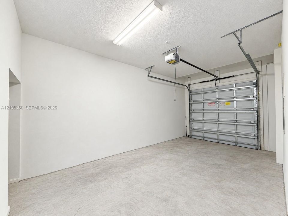 Attached garage featuring a concrete floor, high-clearance ceiling, integrated automatic door opener, and linear fluorescent lighting