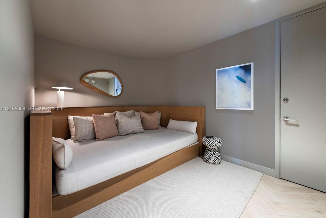 Custom built-in wood bed frame with integrated shelving, light-toned wood-finish flooring in a herringbone pattern, and neutral wall color