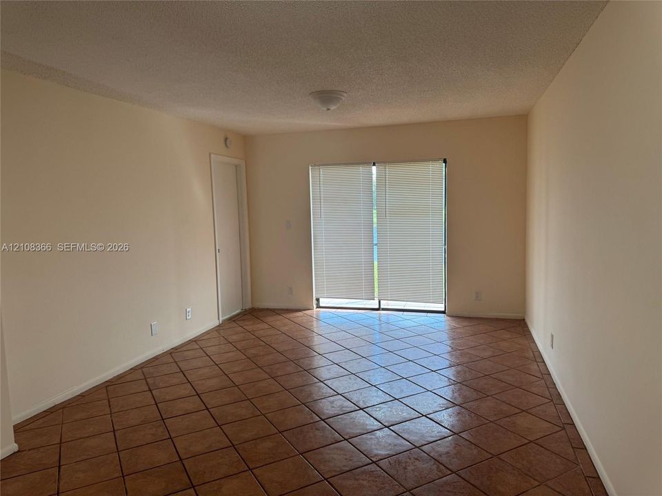 Interior space featuring diagonal ceramic tile flooring, neutral wall tones, a ceiling-mounted light fixture, and sliding glass doors with window blinds