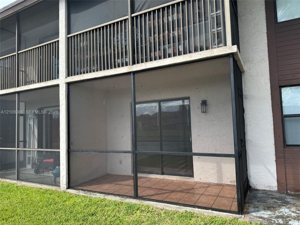 Screened-in lower patio featuring tile flooring, a wall-mounted light fixture, and sliding glass door access, complemented by an upper-level balcony with vertical slat railings