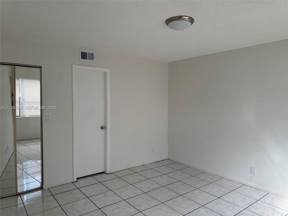 Interior space featuring neutral wall paint, white tile flooring, mirrored closet doors, and a flush-mount ceiling light fixture