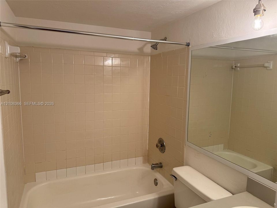 Bathroom featuring a tub and shower combination with tile surround, a large wall-mounted mirror, and a chrome shower fixture