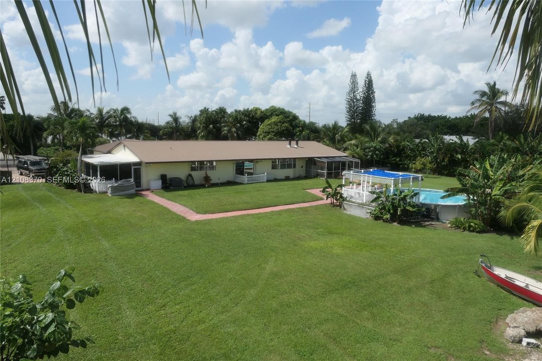 Expansive backyard featuring a large grass lawn, screened-in patio, and an above-ground swimming pool with a hardscape surround