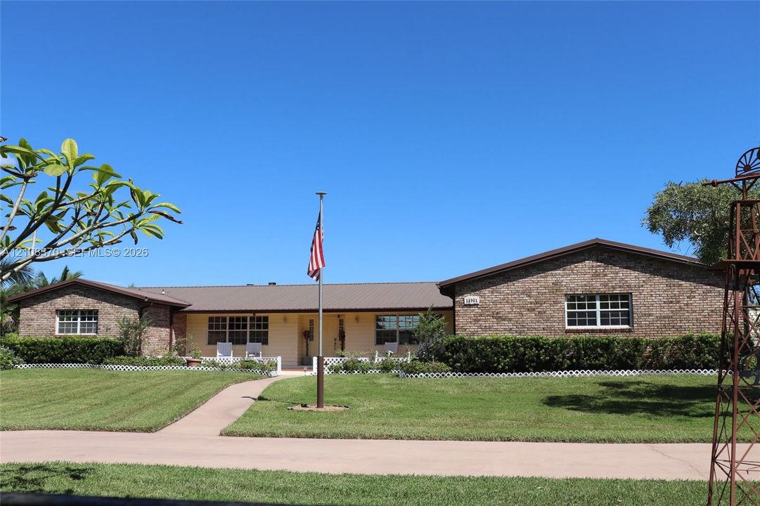 Single-story brick exterior featuring a metal roof, front covered porch, manicured lawn, and ornamental windmill structure