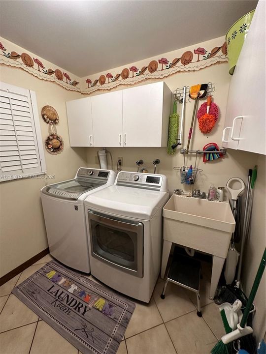 Laundry area featuring white cabinetry, a freestanding utility sink with faucet, ceramic tile flooring, and plantation shutter window coverings