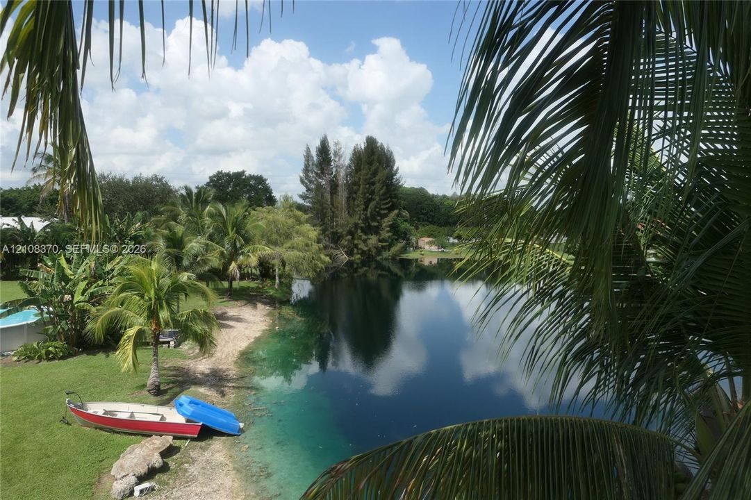Waterfront property featuring a private shoreline, expansive grassy lawn, and mature palm trees