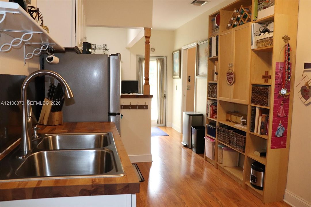 Kitchen featuring a butcher block countertop, stainless steel dual-basin sink with a high-arch faucet, wood-finish flooring, and floor-to-ceiling built-in cabinetry