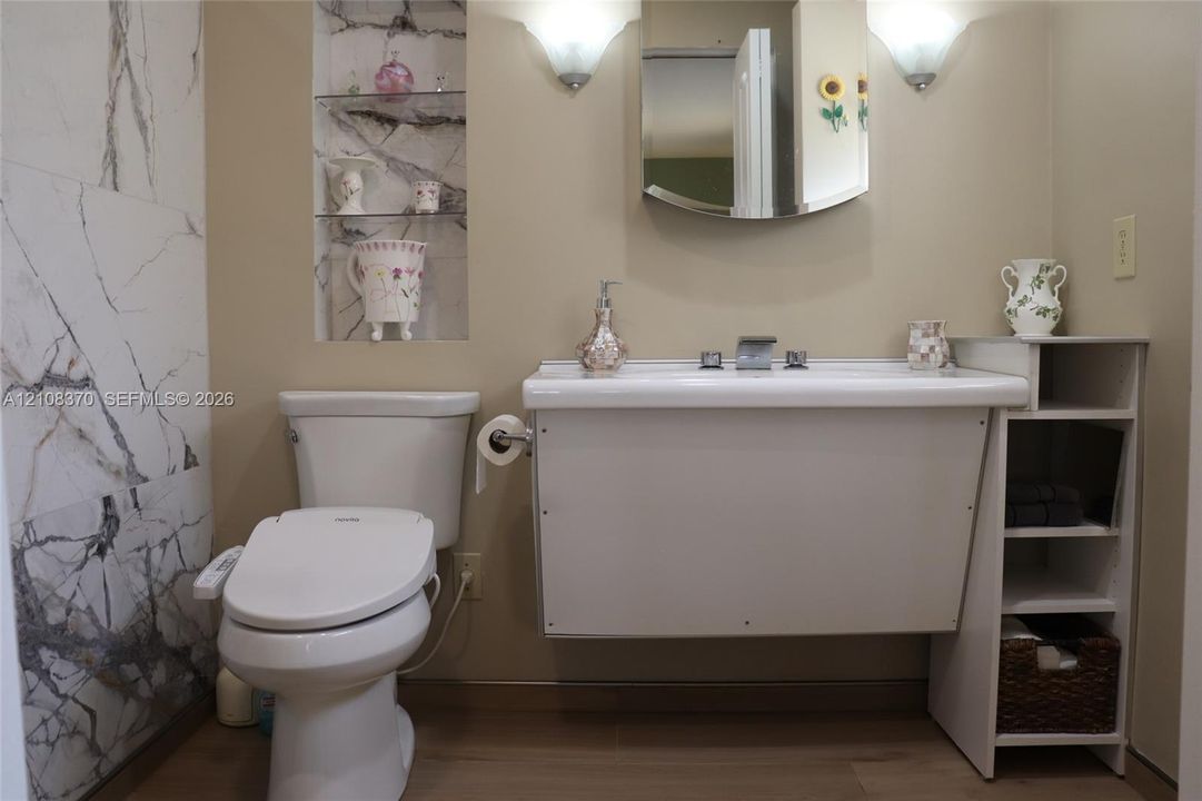 Wall-mounted sink with integrated storage, full-height stone-patterned tile wall, recessed shelving, and dual wall-mounted light fixtures