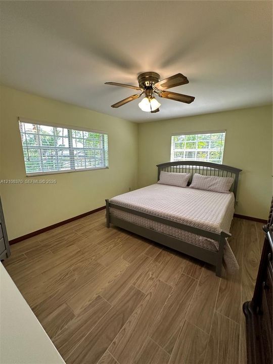 Interior space featuring wood-finish tile flooring, two windows with horizontal blinds, and a multi-blade ceiling fan with integrated lighting