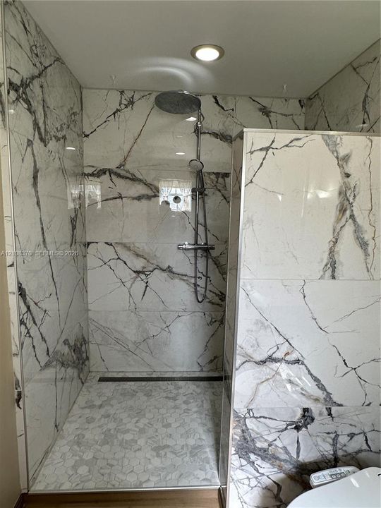 Walk-in shower featuring large-format stone-finish wall tile, hexagonal floor tiling, a rainfall showerhead, and a linear floor drain