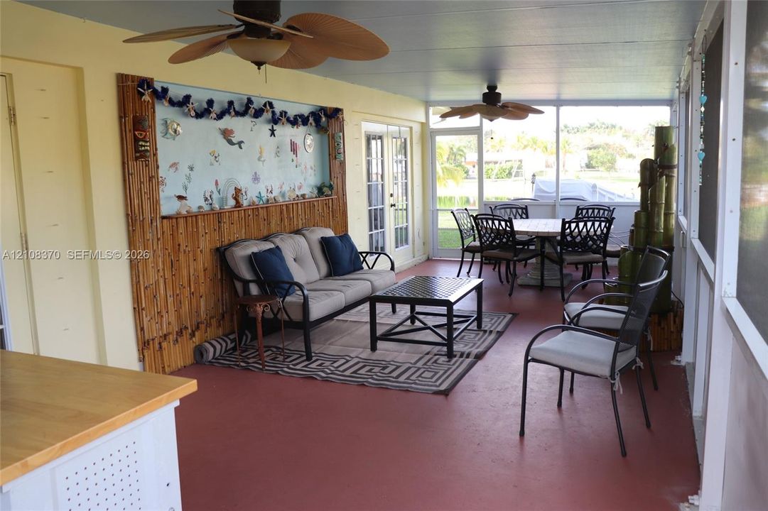 Screened-in porch featuring painted concrete flooring, bamboo-paneled wall accent, dual ceiling fans, and double-door entry