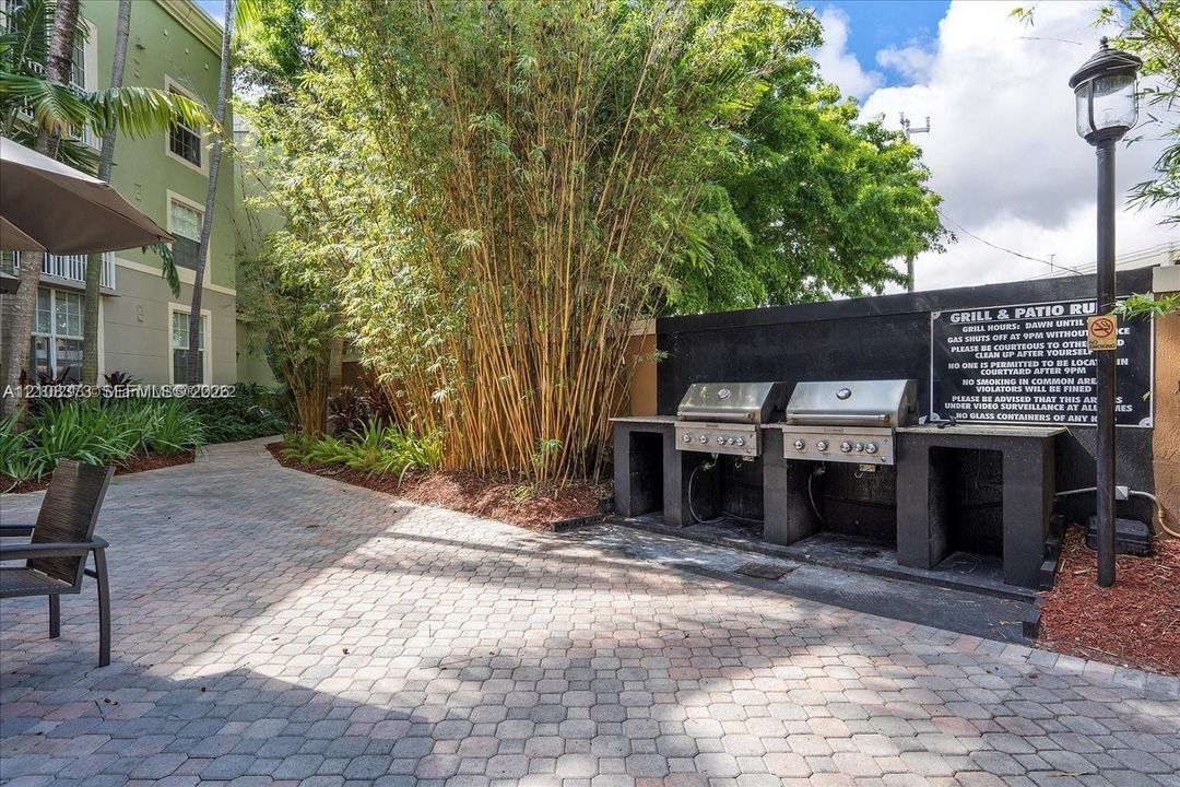 Outdoor common area featuring dual built-in stainless steel gas grills, stone paver patio, and mature bamboo landscaping