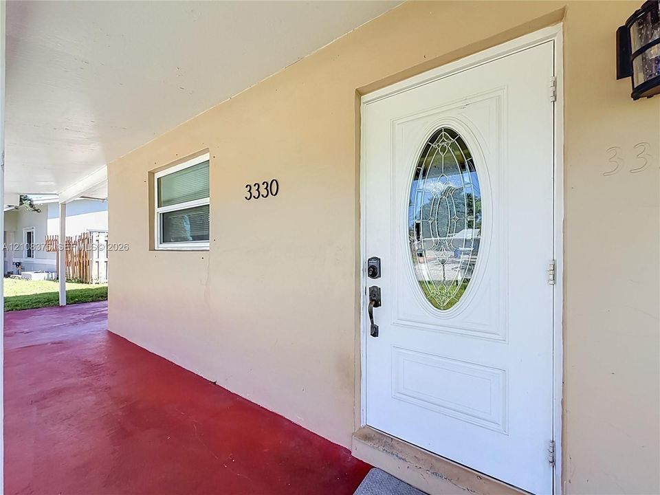 Covered entryway featuring a white paneled door with an oval glass insert, exterior wall-mounted lighting, and a painted concrete porch