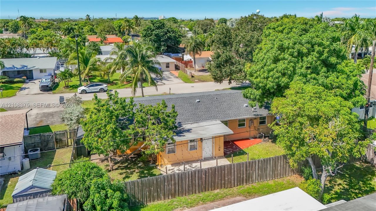 Single-story exterior featuring a shingle roof, concrete patio, perimeter wood fencing, and mature landscaping