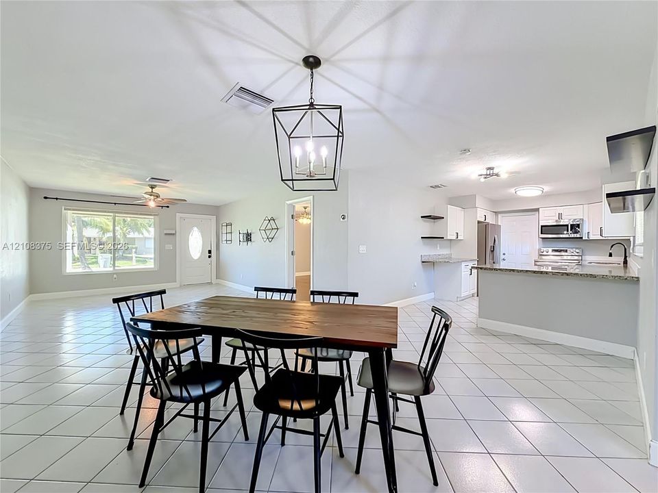 Open-concept interior featuring light-toned tile flooring, kitchen with peninsula counter, built-in cabinetry, and geometric lantern-style pendant lighting