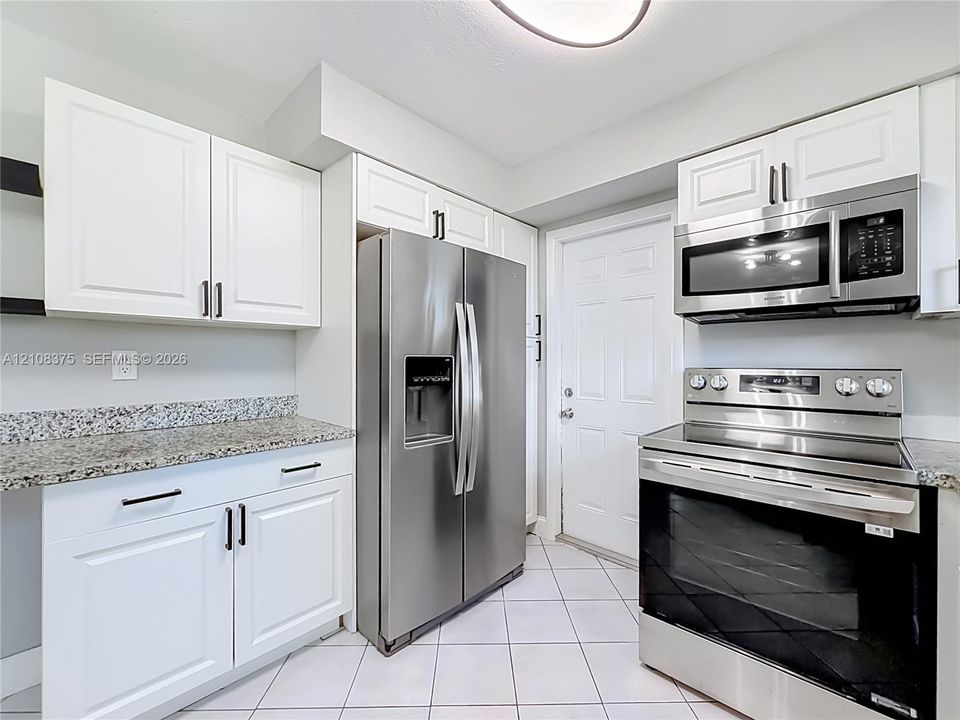 Kitchen featuring white shaker-style cabinetry, stone countertops, stainless steel appliances, and ceramic tile flooring