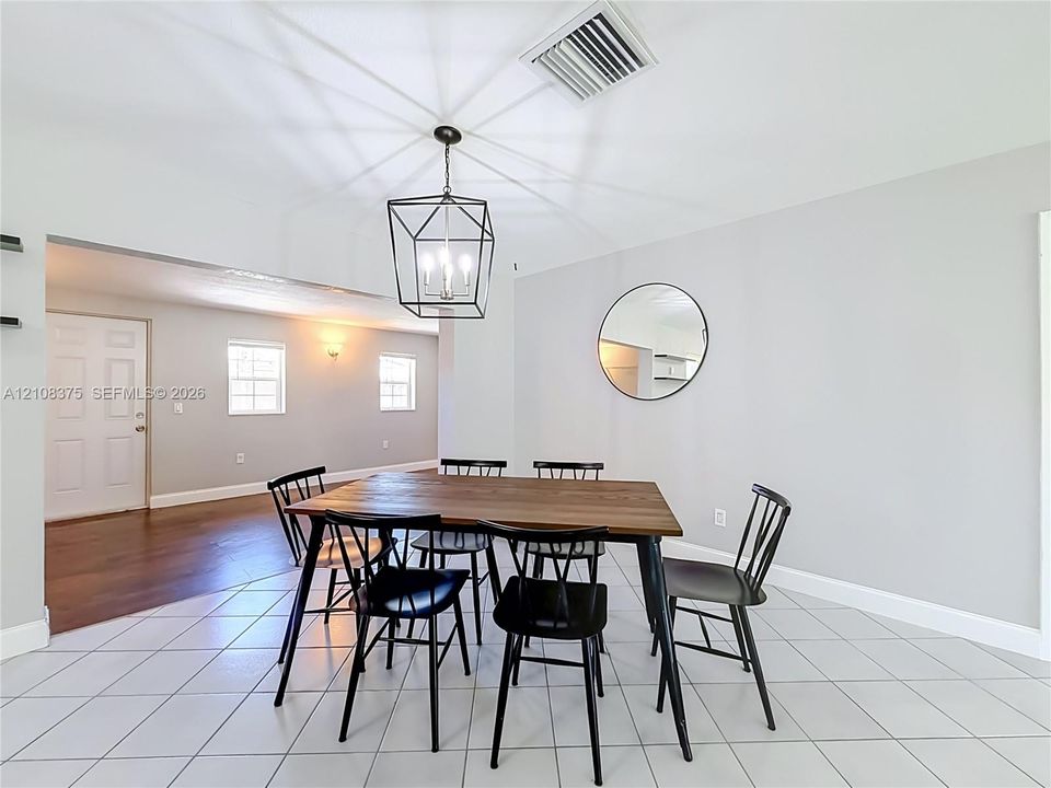 Geometric metal lantern pendant light, circular wall-mounted mirror, neutral interior paint, ceramic tile flooring, and multi-panel solid core door
