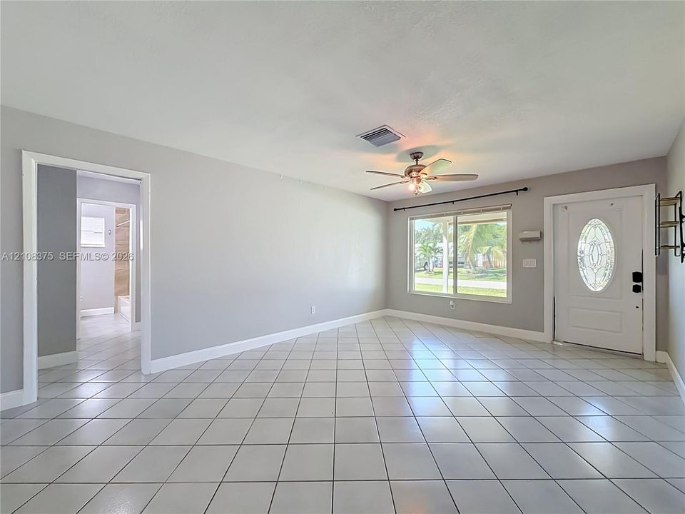Neutral-toned interior space featuring white floor tiles, a ceiling fan with integrated lighting, and an entry door with an oval glass insert