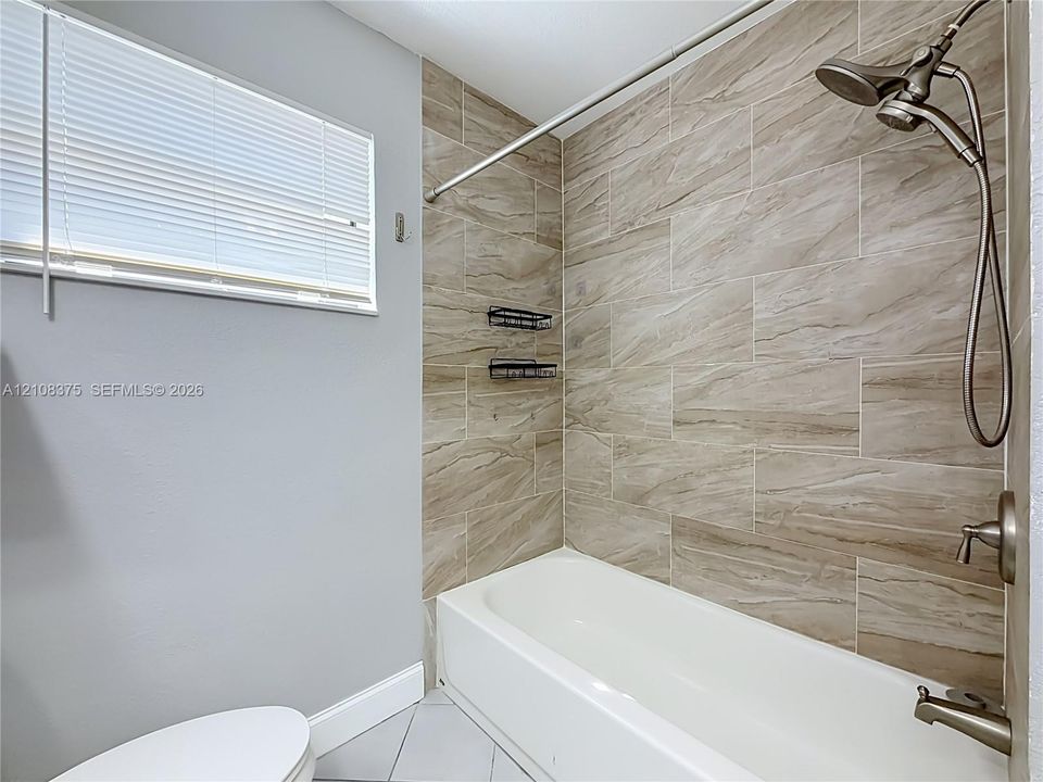 Bathtub featuring large-format ceramic tile surround with natural patterning, brushed-nickel shower hardware, and a horizontal window