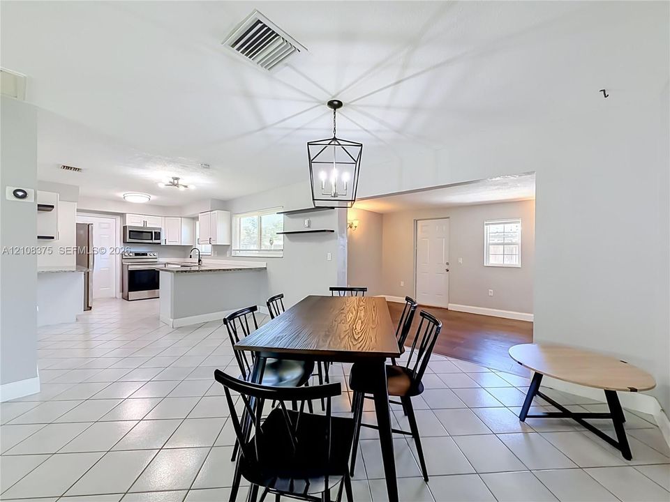 Open-concept floor plan featuring ceramic tile flooring, kitchen with white cabinetry, stone-finish countertops, stainless steel appliances, and a geometric metal pendant light fixture