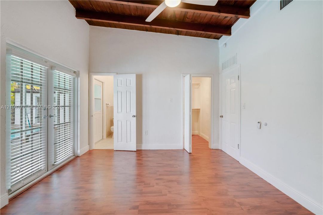 Another view from within the primary bedroom with vaulted ceiling with exposed wood beams, wood-finish flooring, dual French doors, and ceiling-mounted light/fan fixture