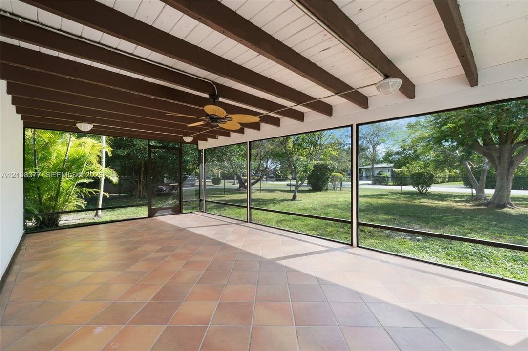 Screened patio featuring ceramic tile flooring, exposed wooden ceiling beams, and a mounted ceiling fan
