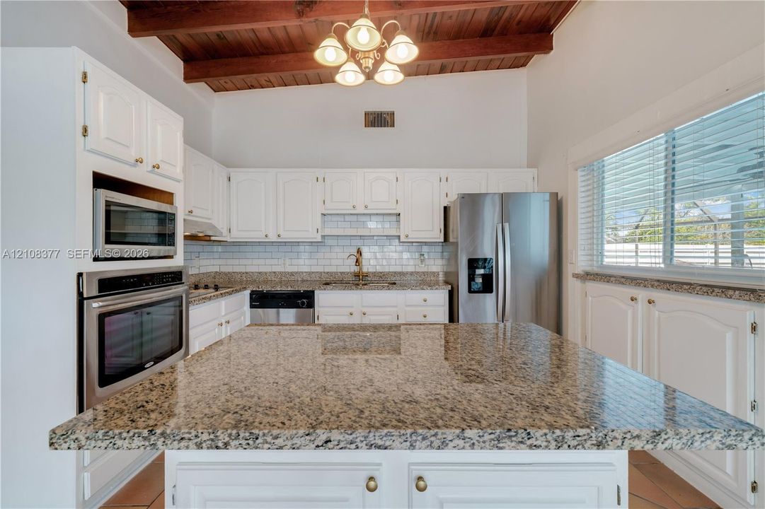 Kitchen featuring white cabinetry, granite countertops, stainless steel appliances, a subway tile backsplash, and vaulted ceiling with exposed wood beams