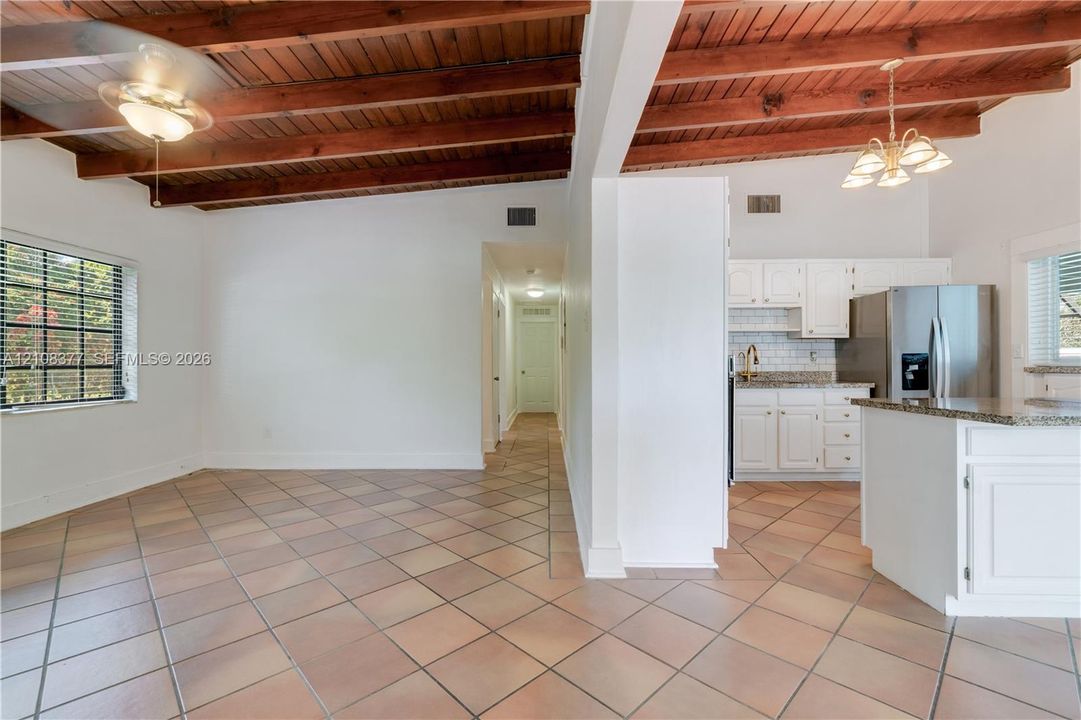Vaulted ceilings with exposed wooden beams, ceramic tile flooring, kitchen featuring granite countertops, subway tile backsplash, and ceiling-mounted light fixtures