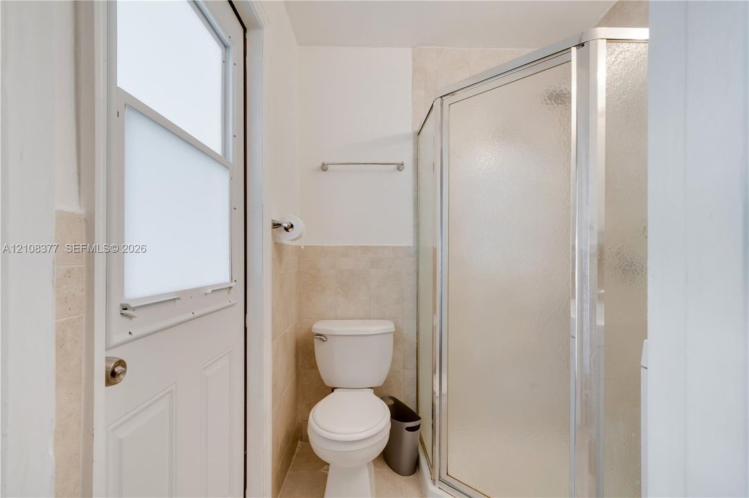 Corner shower enclosure with textured glass doors, tile wall accents, and an exterior-access door featuring a frosted glass window