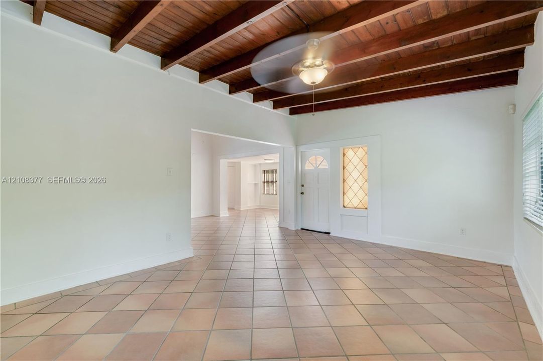 View from within the living room with exposed wood ceiling beams, ceramic tile flooring, and entry door with decorative glass sidelight