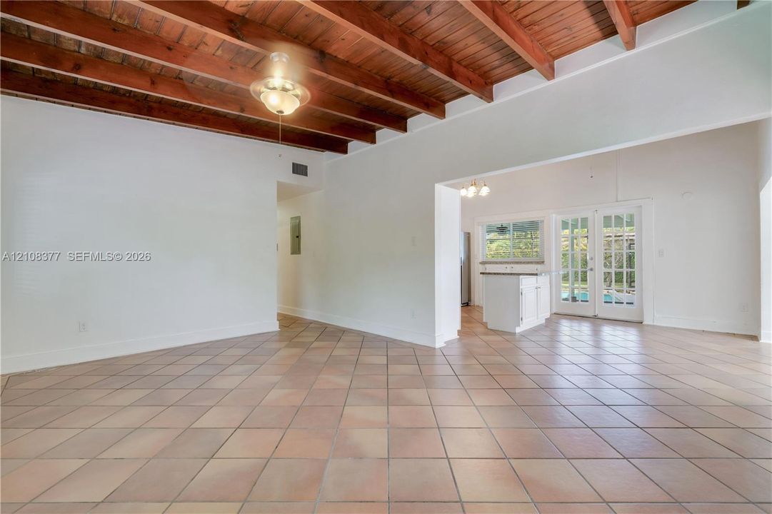 Vaulted ceiling featuring exposed wood beams, ceramic tile flooring, and French doors in the background