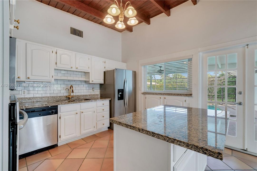 Kitchen featuring exposed wood-beam ceilings, white cabinetry, granite countertops, subway tile backsplash, and ceramic tile flooring * views to the pool & patio.