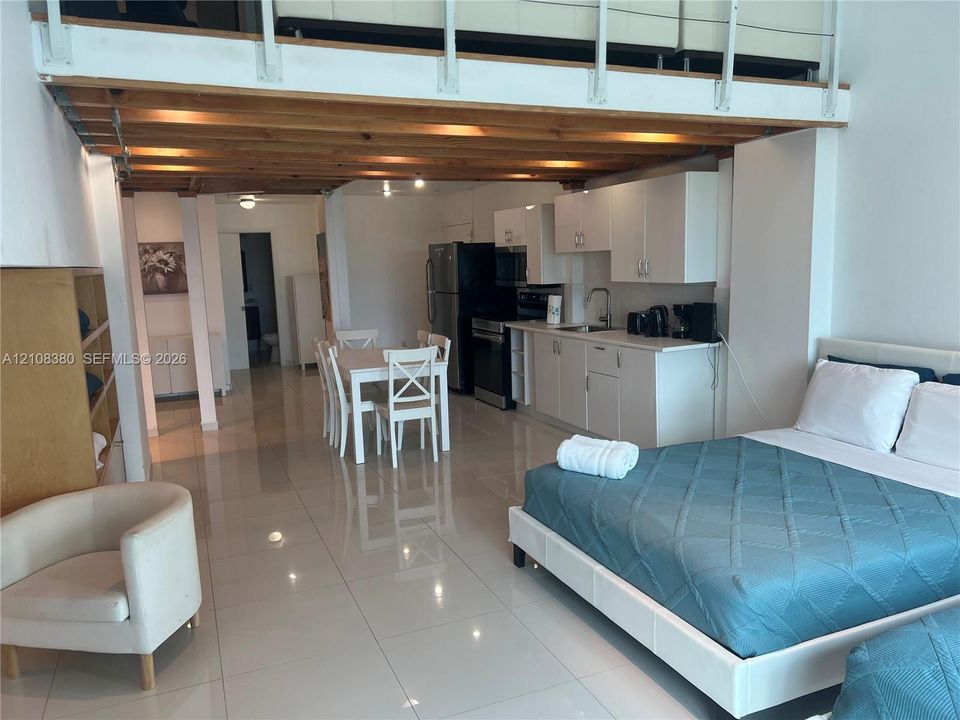High-ceiling interior featuring an exposed wood-beam loft structure, polished tile flooring, white cabinetry, and recessed lighting