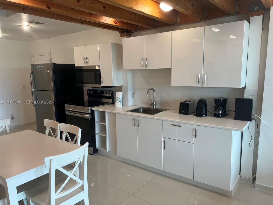 Kitchen featuring high-gloss white cabinetry, white stone-finish countertops, exposed wooden ceiling beams, and polished tile flooring
