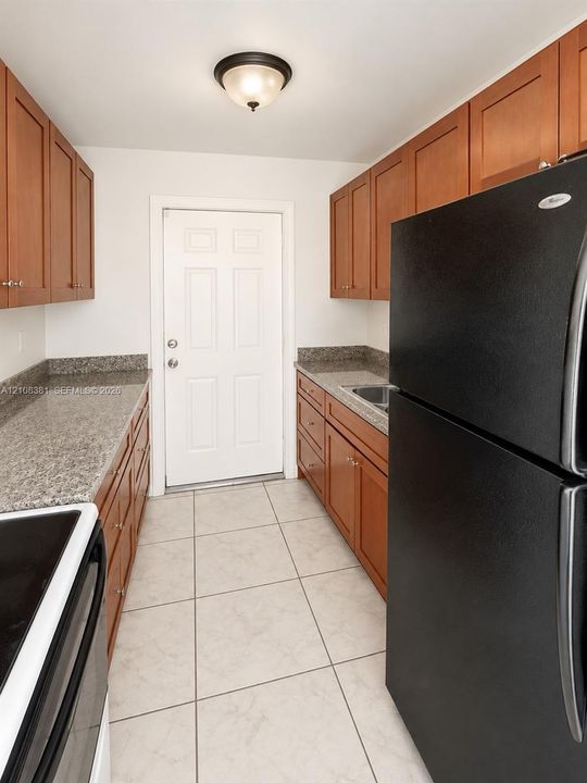 Kitchen featuring wood cabinetry, stone-finish countertops, tile flooring, and a flush-mount ceiling fixture