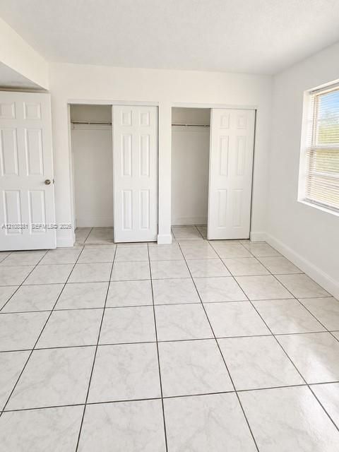 Neutral tile flooring, dual reach-in closets with six-panel doors, and a double-hung window with integrated blinds