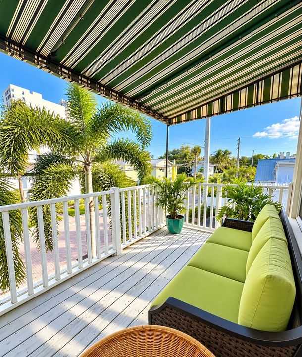 Covered balcony featuring white railing, light-toned wood-finish flooring, and a retractable striped awning
