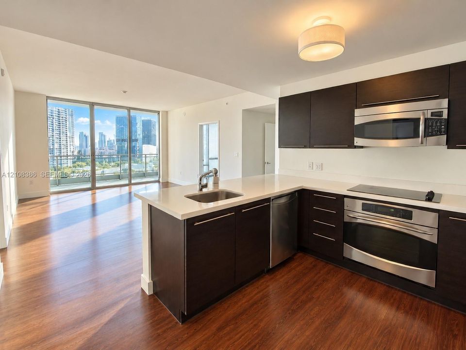Kitchen featuring dark cabinetry, solid-surface countertops, integrated stainless steel appliances, and wood-finish flooring with floor-to-ceiling windows