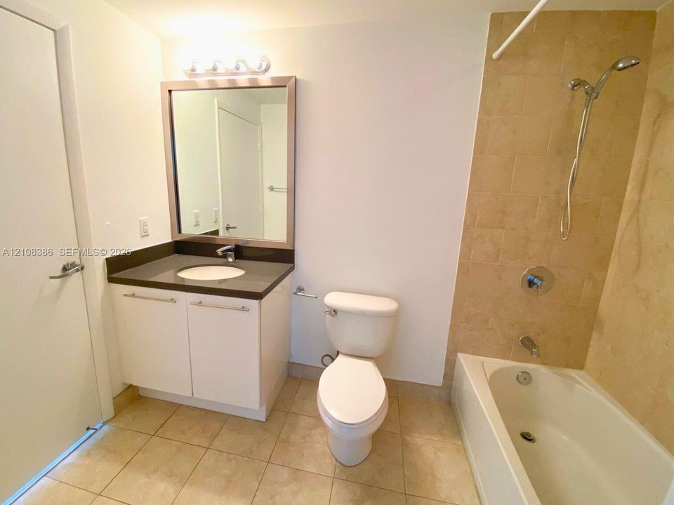 Bathroom featuring white cabinetry, solid-surface countertop, rectangular mirror with brushed-finish frame, and tub enclosure with tile surround