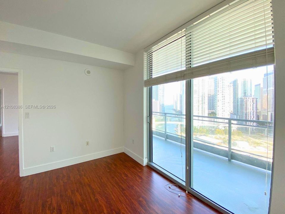 Floor-to-ceiling windows, wood-finish flooring, and a glass-paneled balcony with urban and water scenery