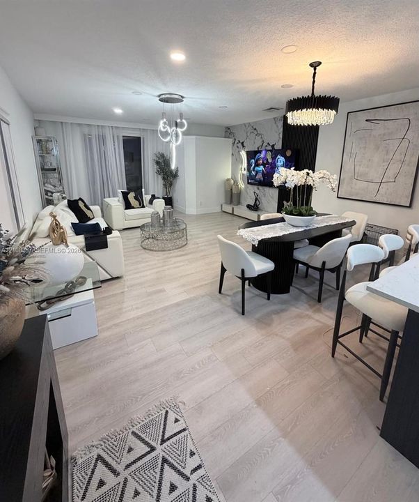 Light-toned wood-finish flooring, accent wall with stone-finish cladding and black vertical paneling, tiered modern chandelier, crystal drum pendant lighting, and recessed ceiling lighting
